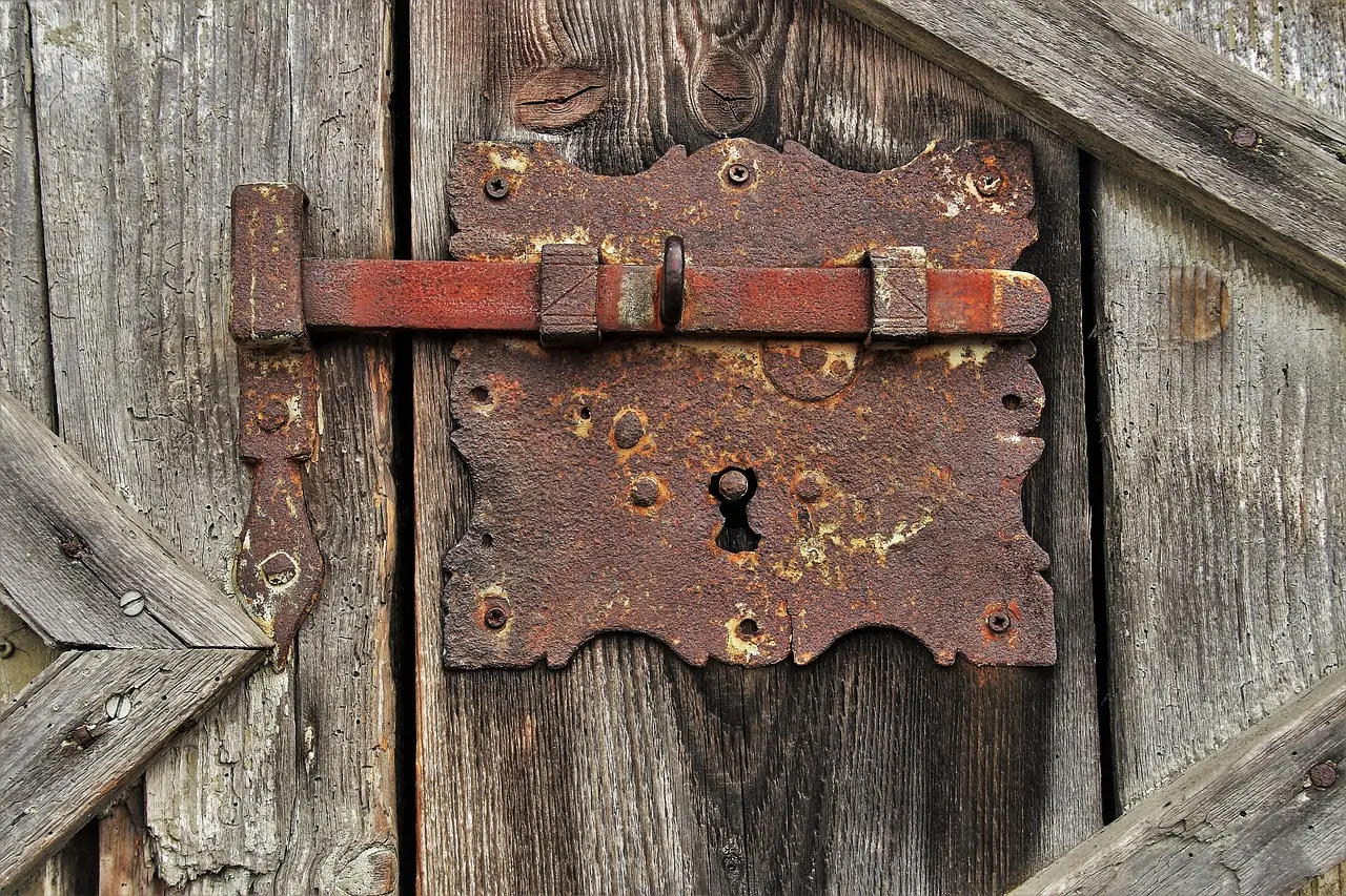 A rusty iron latch and keyhole plate on an old weathered wooden door
