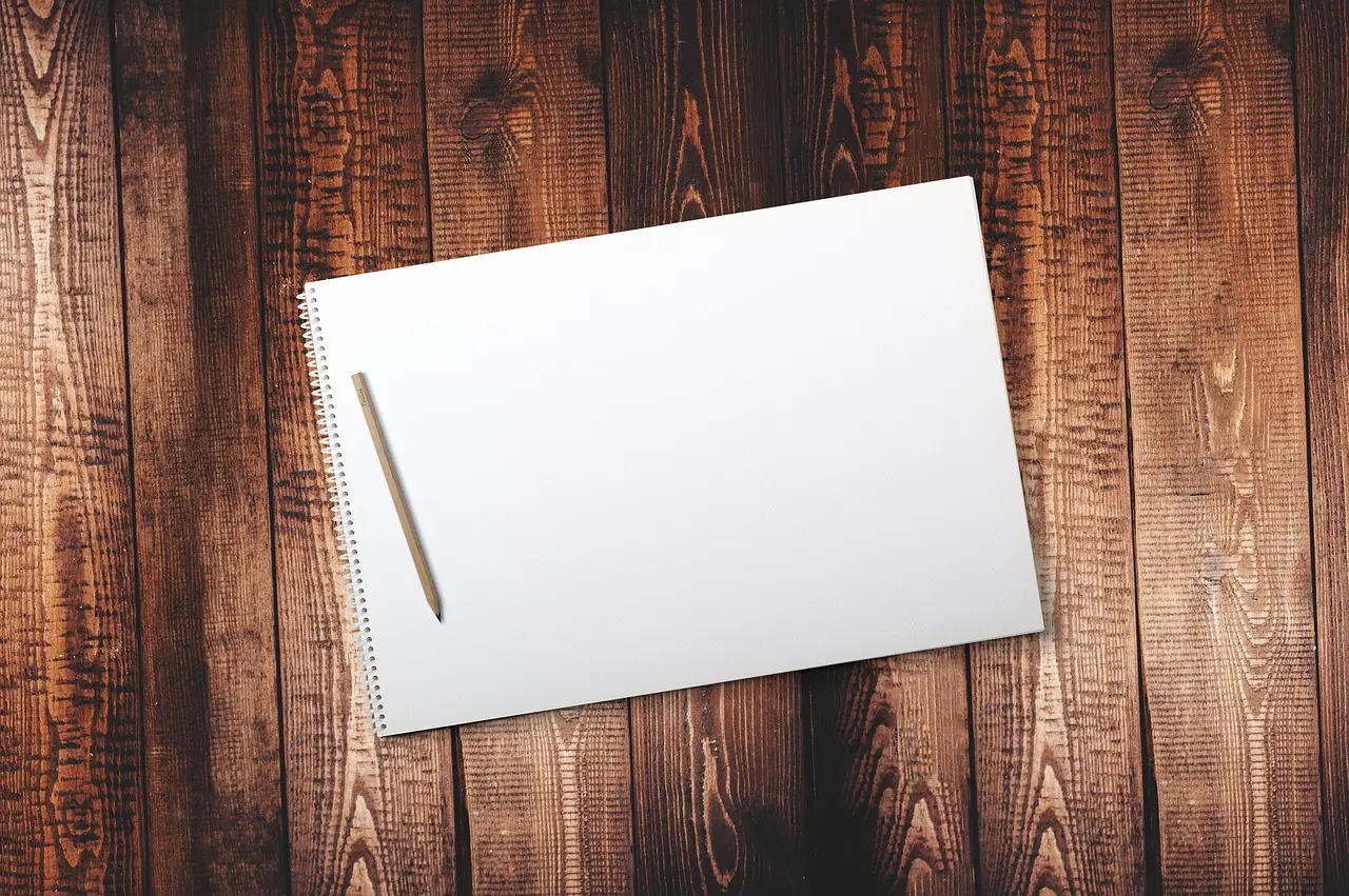 A blank spiral sketchbook with a pencil on dark wooden boards, seen from above