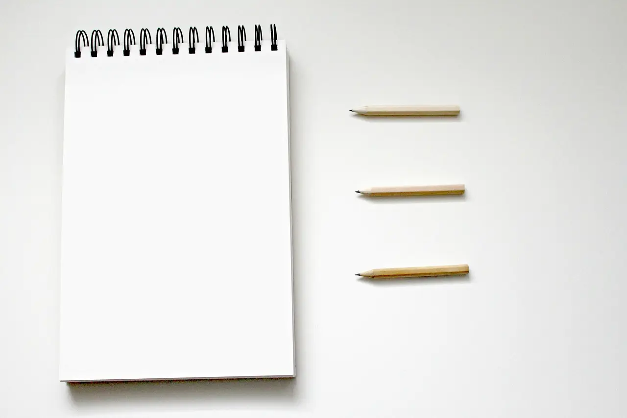 A blank spiral notebook beside three pencils